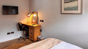 Een slaapkamer met een bed, een bureau met lamp, een stoel, een televisie en een lijst aan de muur.