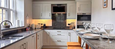 A modern kitchen with white cabinetry, a granite countertop, wooden stools, and a dining table set for six.
