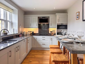 Una cocina moderna con armarios blancos, encimera de granito, taburetes de madera y una mesa de comedor preparada para seis personas.
