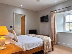 A bedroom with a bed, bedside table, lamp, TV, window, and curtains.