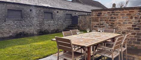 A rustic outdoor dining area with a stone wall, a wooden table, and chairs.