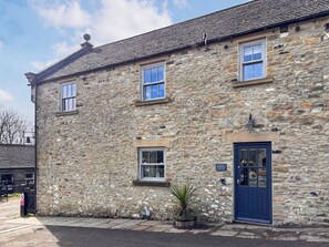 A stone building with a blue door, two windows, and a sign that reads 'Stable Cottage.'