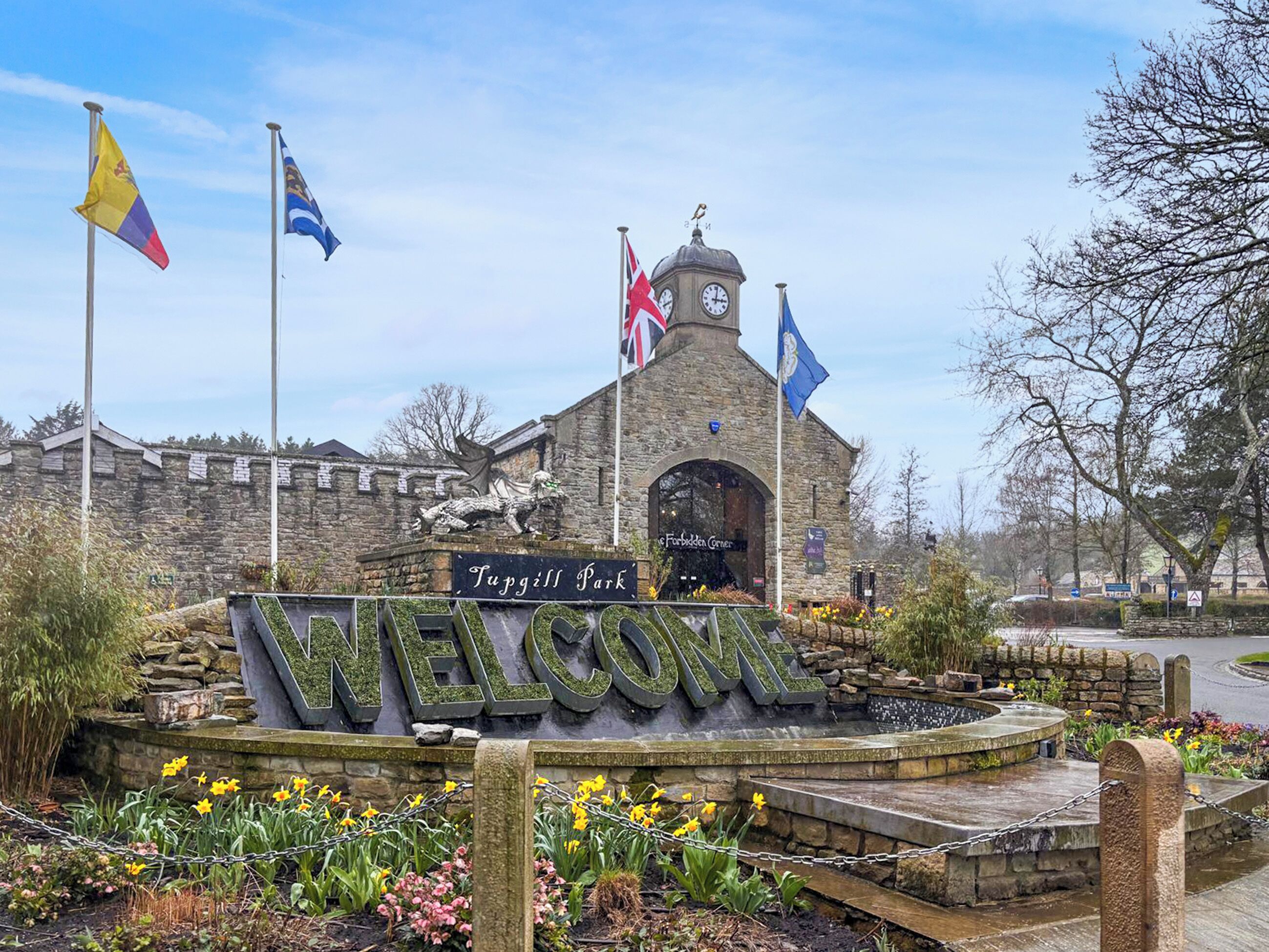 A stone building with a clock tower, flags, and a 'Welcome' sign.