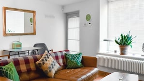 A living room with a brown leather sofa, a table with glasses, a potted plant, a mirror, and a radiator.