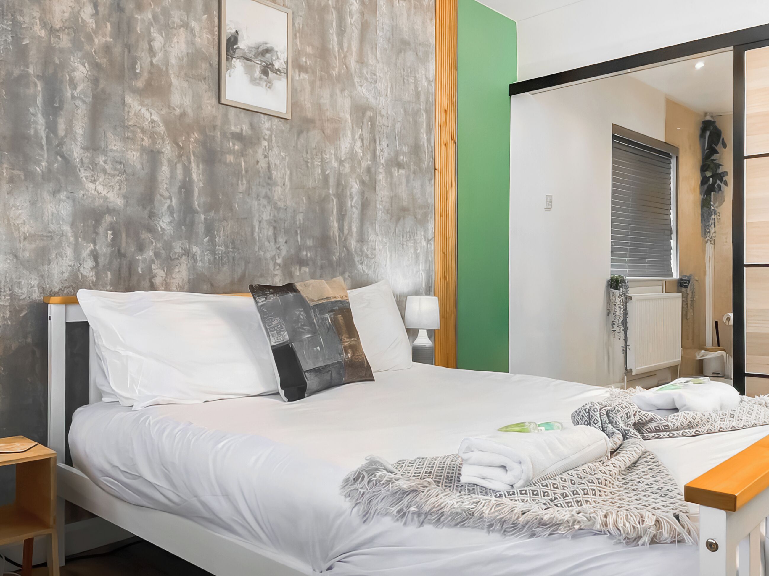 Une chambre d’hôtel moderne, équipée d’un lit, d’une table de chevet, d’une lampe et offrant une vue sur la salle de bain.