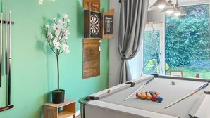 A pool table with balls, a dartboard, a potted plant, and a window with a view of greenery. - 5 bedroom accommodation in Pudsey, near Leeds (Pudsey, near Leeds)