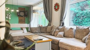 A living room with a sectional sofa, a coffee table, a wall-mounted lamp, and a window with curtains. - 5 bedroom accommodation in Pudsey, near Leeds (Pudsey, near Leeds)