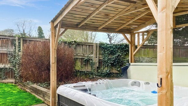A hot tub under a wooden pergola in a backyard with a wooden fence and greenery. - 5 bedroom accommodation in Pudsey, near Leeds (Pudsey, near Leeds)