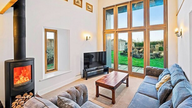 A living room with a fireplace, a sofa, a TV, and large windows. - 5 bedroom accommodation in Shepton Mallet (Shepton Mallet)