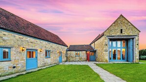 A stone building with a red-tiled roof, a blue door, and a paved courtyard. - 5 bedroom accommodation in Shepton Mallet (Shepton Mallet)