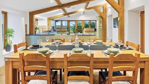 A dining area with a wooden table set for six, a kitchen in the background, and a view of the outdoors. - 5 bedroom accommodation in Shepton Mallet (Shepton Mallet)