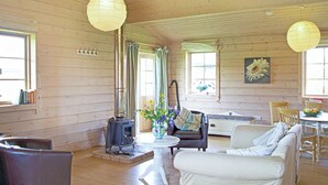 A cozy cabin interior with a fireplace, wooden walls, a sofa, and a dining area. - Curlew Lodge - UK51677 (Dumfries and Galloway)