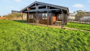 A wooden cabin with a porch, a dining area, and a view of a grassy field. - Curlew Lodge - UK51677 (Dumfries and Galloway)