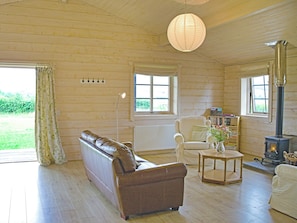 A wooden interior with a sofa, armchair, table, and a wood-burning stove.