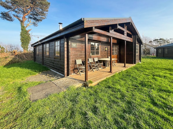 A wooden cabin with a covered porch, a table with chairs, and a sign reading 'Skyark Lodge.'