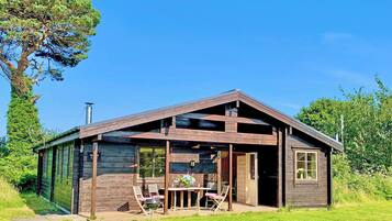 A wooden cabin with a porch, a table, and chairs.
