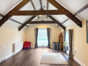 A loft-style room with exposed wooden beams, a large window with curtains, a radiator, and a red sofa.