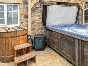 Un mur extérieur en pierre, un tonneau en bois, un jacuzzi et un banc en bois.