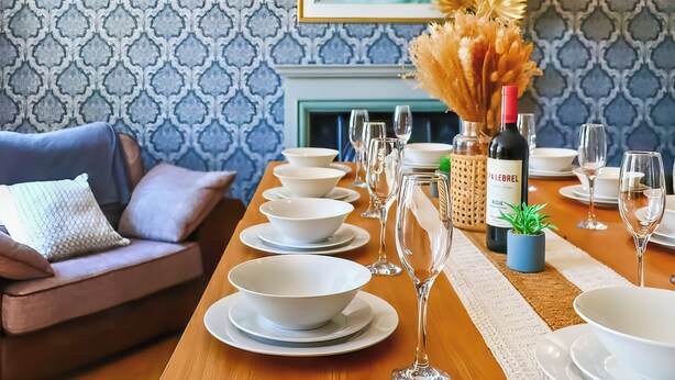 A dining table set with white plates, bowls, and wine glasses, a bottle of CÎTELIER wine, and a small potted plant.