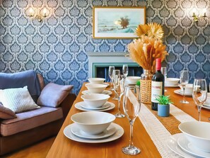 Una mesa de comedor dispuesta con platos, tazones y copas de vino blancos, una botella de vino CÎTELIER y una pequeña planta en maceta.