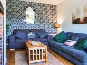 Ett vardagsrum med mönstrat tapet, en spegel, en soffa, ett soffbord och en lampa.