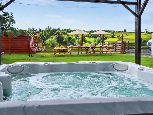 Un jacuzzi con vistas a un área verde, mesas de picnic y una valla de madera.