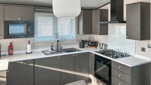 Une cuisine moderne dotée d’un îlot central, d’appareils électroménagers en acier inoxydable et d’un luminaire suspendu.