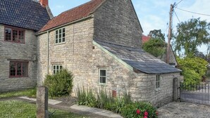 A stone house with a sloped roof, a chimney, and a small garden with flowers. - 1 bedroom accommodation in Somerset, Glastonbury, Street, Shepton Mallet (Somerset, Glastonbury, Street, Shepton Mallet)