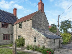 A stone house with a sloped roof, a chimney, and a small garden with flowers. - 1 bedroom accommodation in Somerset, Glastonbury, Street, Shepton Mallet (Somerset, Glastonbury, Street, Shepton Mallet)