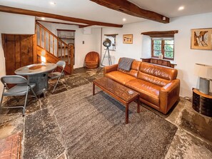A living room with a brown leather sofa, a coffee table, a dining table with chairs, and a stone-tiled floor. - 1 bedroom accommodation in Somerset, Glastonbury, Street, Shepton Mallet (Somerset, Glastonbury, Street, Shepton Mallet)