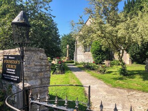 A church entrance with a sign, a stone pathway, and surrounding greenery. - 1 bedroom accommodation in Somerset, Glastonbury, Street, Shepton Mallet (Somerset, Glastonbury, Street, Shepton Mallet)
