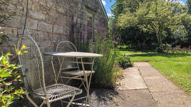A stone building with a garden path, outdoor seating with metal chairs and a table, and a variety of plants and flowers. - 1 bedroom accommodation in Somerset, Glastonbury, Street, Shepton Mallet (Somerset, Glastonbury, Street, Shepton Mallet)