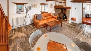 A cozy living room with a leather sofa, a stone fireplace, and a dining area with a table and chairs. - 1 bedroom accommodation in Somerset, Glastonbury, Street, Shepton Mallet (Somerset, Glastonbury, Street, Shepton Mallet)