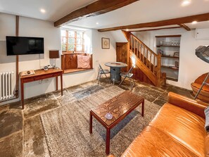 Ein Wohnzimmer mit Steinfußboden, Holzmöbeln, einem Fernseher, einer Treppe und einem Fenster mit Jalousien.