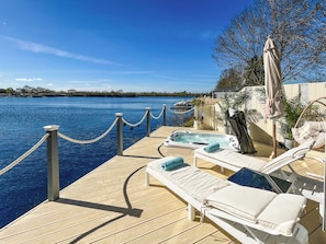 A wooden deck with lounge chairs and a hot tub overlooking a body of water.