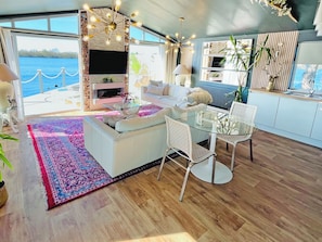 A modern living room with a fireplace, a glass coffee table, and a view of the water.