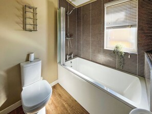 A bathroom with a toilet, a shower with a glass door, and a window with blinds. - 1 bedroom accommodation in Tallington (Tallington)