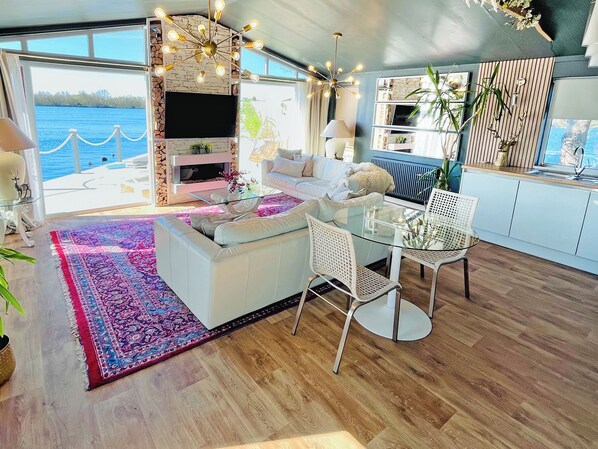 A modern living room with a fireplace, a glass coffee table, and a view of the water.