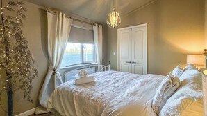 Un dormitorio con cama, ventana, puerta y lámpara colgante.