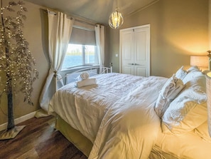 A bedroom with a bed, a window, a door, and a hanging light fixture.