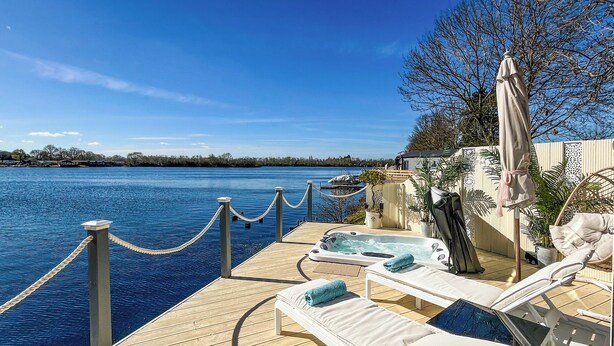 Terraza de madera con sillones de descanso y jacuzzi con vistas a una masa de agua.