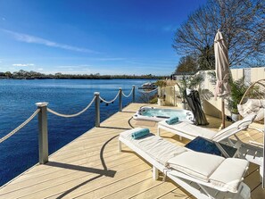 A wooden deck with lounge chairs and a hot tub overlooking a body of water. - 1 bedroom accommodation in Tallington (Tallington)