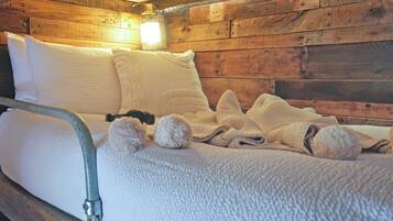 A bed with white bedding, a metal headboard, and a wooden wall with a light fixture.