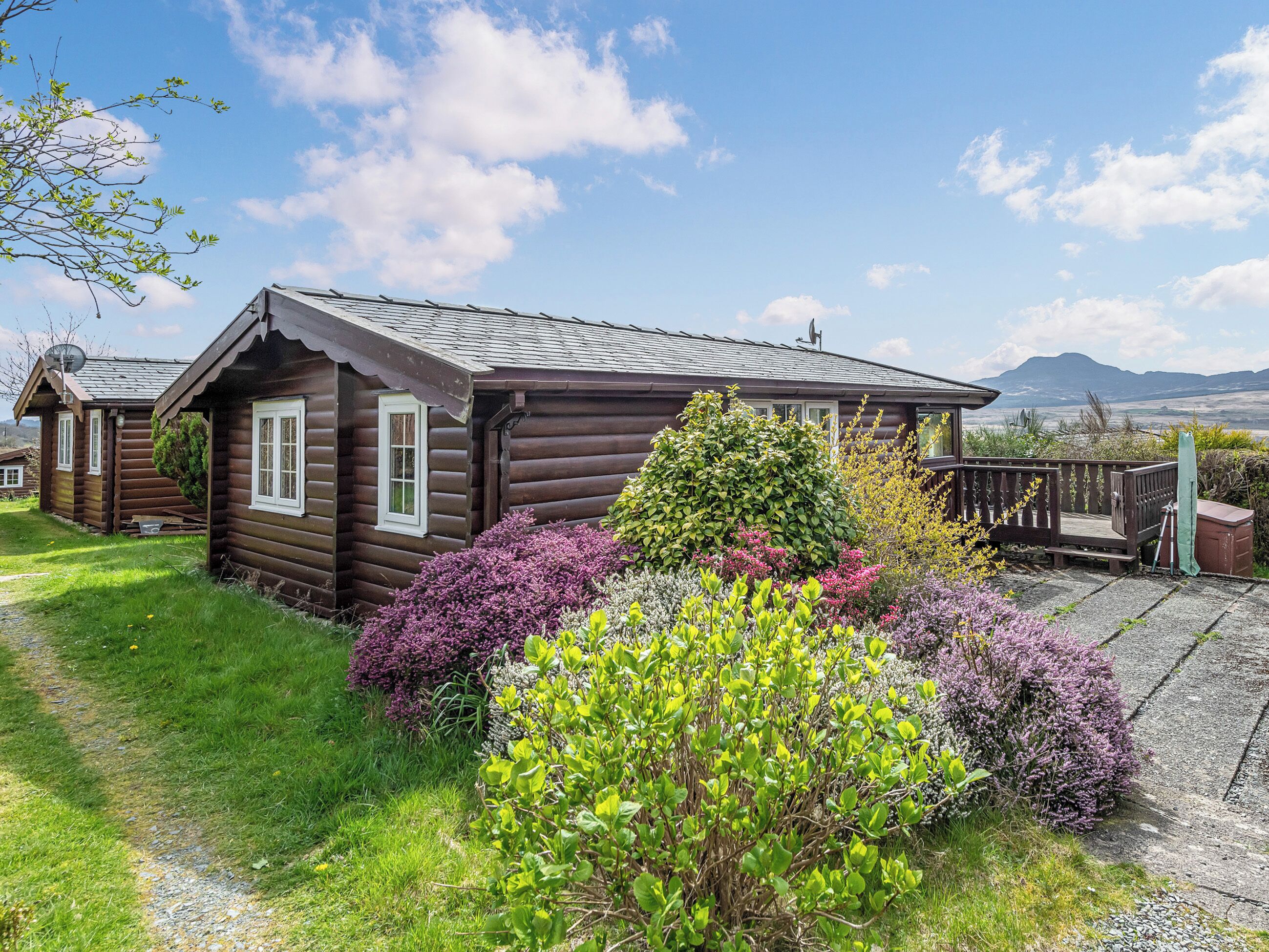 Eine Blockhütte mit einer Terrasse, umgeben von üppigem Grün und wolkenlosem Himmel.