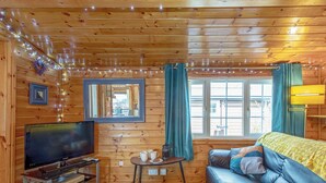A wooden cabin interior with a television, sofa, and window with curtains. - 2 bedroom accommodation in Trawsfynydd (Trawsfynydd)