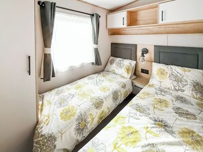Ein kleines Schlafzimmer mit zwei Betten, einem Fenster mit Vorhängen, einem Nachttisch und eingebauten Schränken.