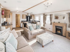 A spacious living room with a sofa, ottoman, and fireplace. There is a kitchen area with a stove and cabinets. - Platinum Collection - 3 - UK51704 (Sandown)