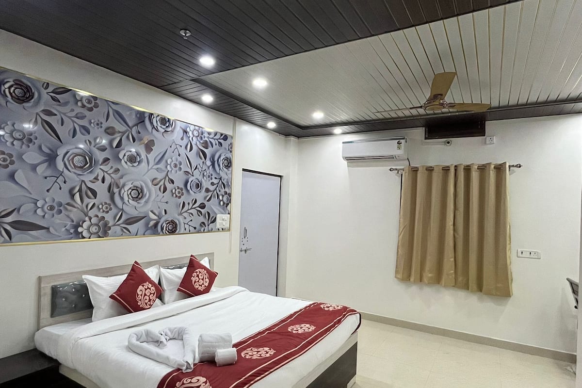 Habitació d'hotel amb llit, ventilador de sostre, aparell d'aire condicionat i un panell decoratiu a la paret.