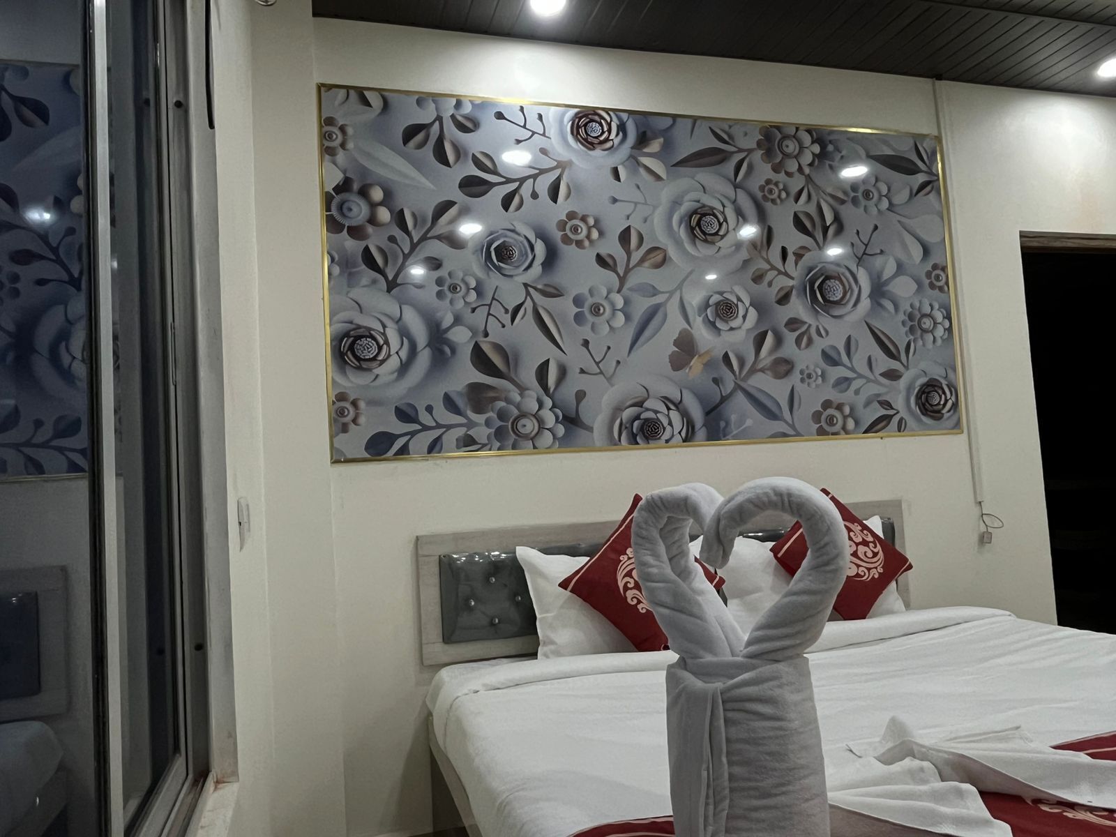 A hotel room with a bed, a decorative wall panel, and a towel rack with towels.