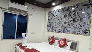 Ein ordentlich bezogenes Bett mit einer rot-weißen Tagesdecke, eine Wand mit floralem Wandpapier und ein Fenster mit Vorhang.